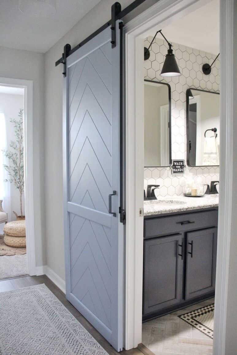A black and white bathroom with accentuating blue-gray herringbone chevron barn door