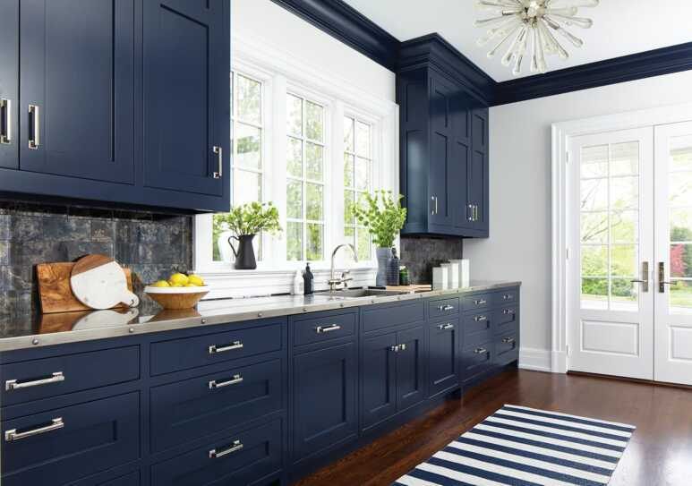 A contemporary kitchen with navy blue kitchen cabinetry paired with navy blue and white striped rug and sputnik chandelier with glass accent