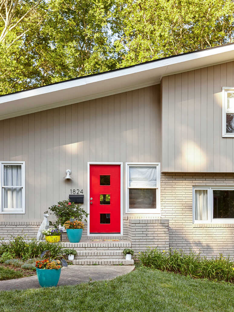 A crimson red front door with three square glass panels in a cream tan vertical siding house