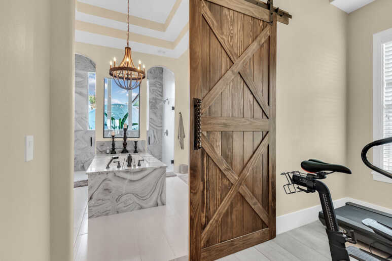 A luxurious spa-like design with wooden barn door and marble arrangements in a transitional bathroom