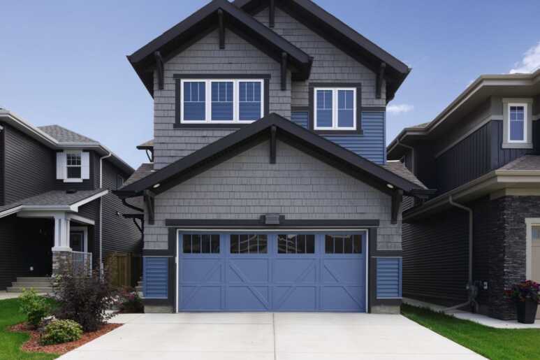 A modern barn garage door painted in Kashmir blue with a grey exterior and dark gable roof