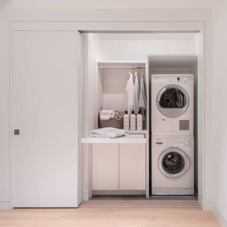 A multi-panel telescopic door in an all-white laundry closet for a large opening in a small laundry closet