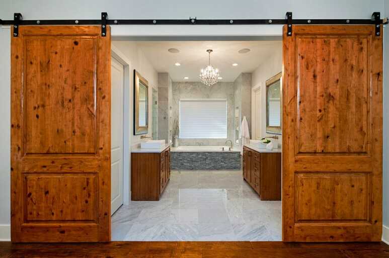 Double oak barn door leads to a grand and luxurious bathroom