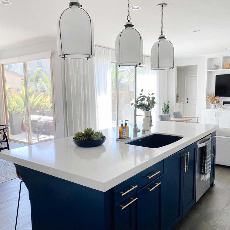 Elegant navy blue freestanding kitchen cabinets in an all-white room with greenery on top