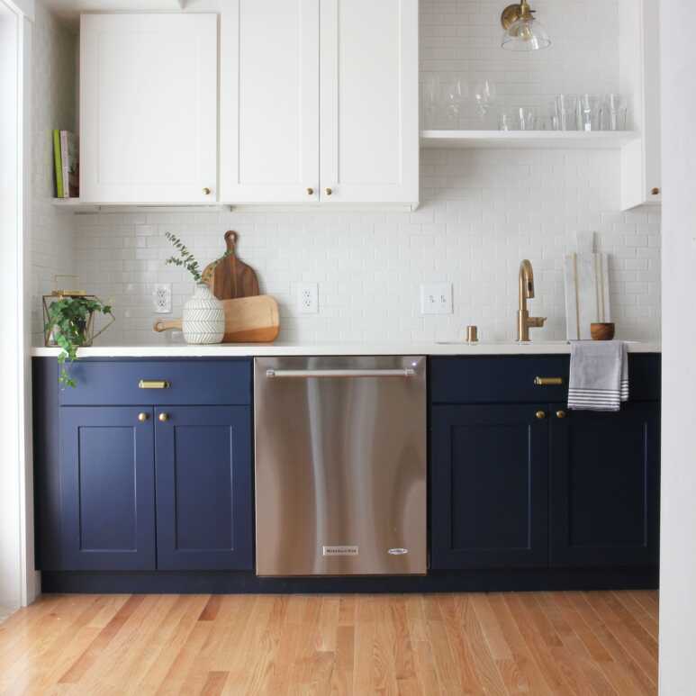 Navy blue base kitchen cabinets in a minimalist kitchen with white wall cabinets and light brown flooring for a natural atmosphere