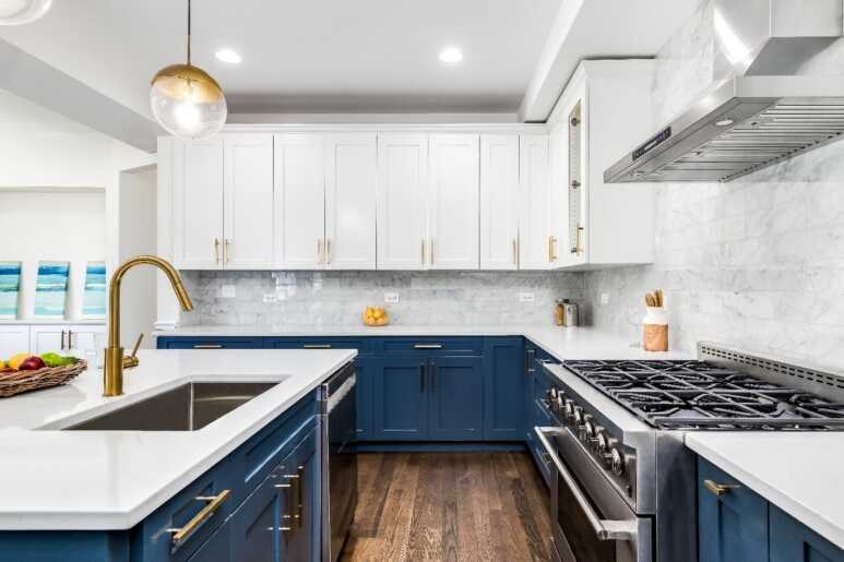 Navy blue kitchen cabinets combined with white marble walls, brown wooden floor, and golden fixtures for a luxurious kitchen