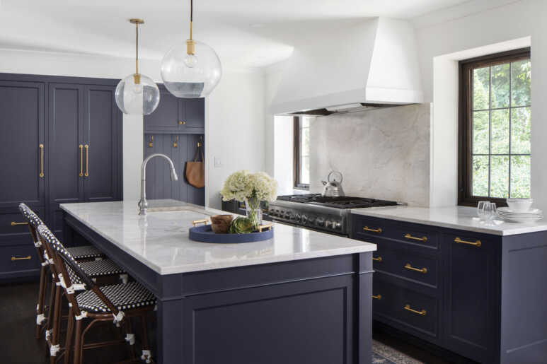 Navy blue kitchen cabinets in darker shade combined with dark brown furniture and golden fixtures create a neutral vibe