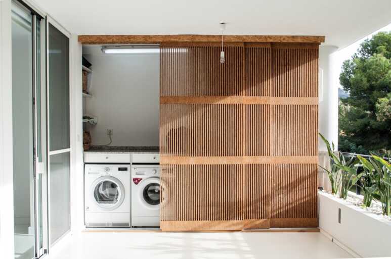 The multi-slide pocket door with wooden slats enhances the natural atmosphere for the balcony laundry room