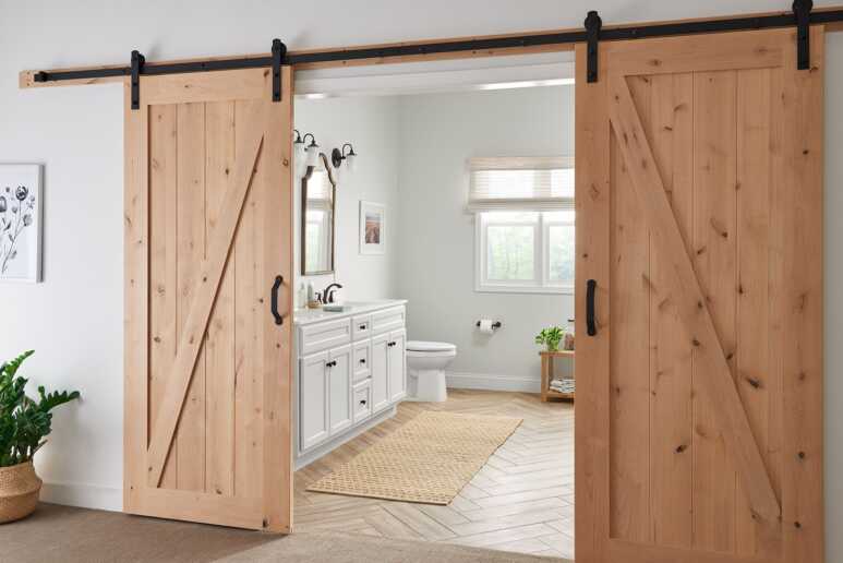 The wood and greenery ornaments in a farmhouse bathroom intensify a wood barn door's minimalist and natural vibe